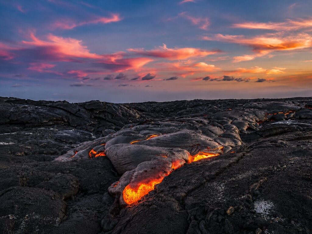 Glowing lava flowing across black volcanic rock at sunset in Hawaii Volcanoes National Park, Big Island